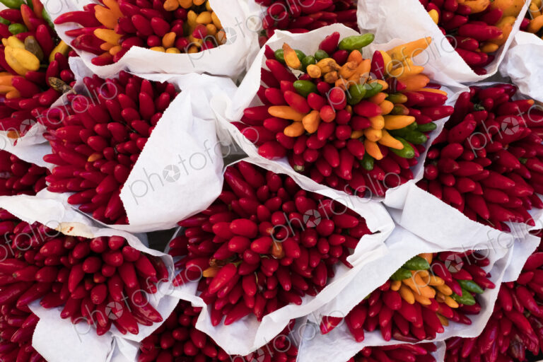 High angle close up of a large bunches of fresh red and orange chillies at a market stall.