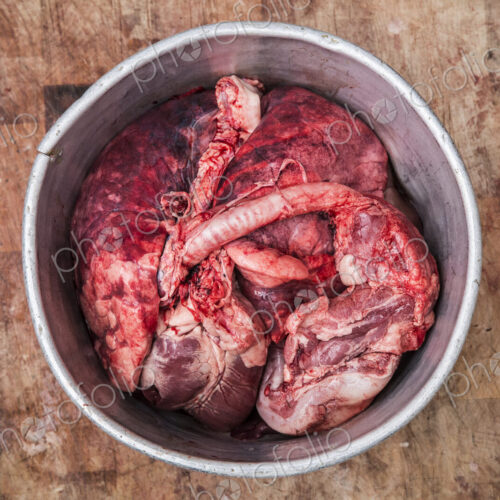 High angle close up of a metal bucket with meat and offal standing on a wooden…