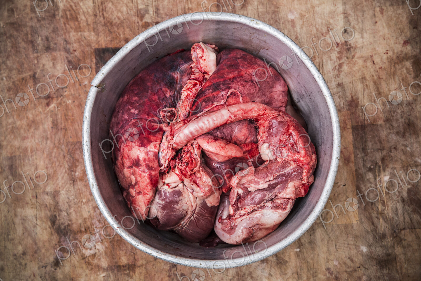 High angle close up of a metal bucket with meat and offal standing on a wooden…