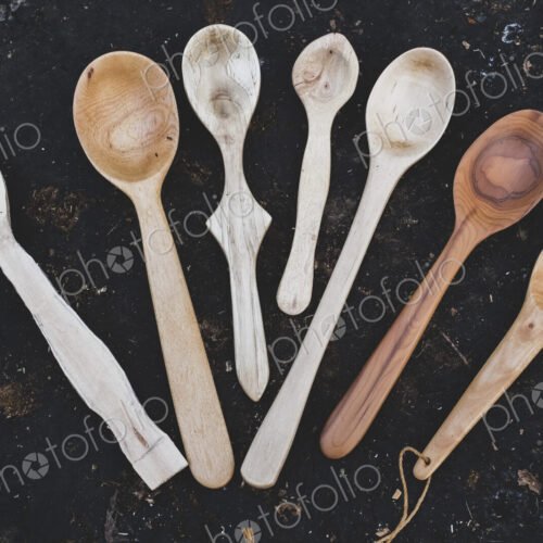 High angle close up of a selection of carved wooden spoons on chopping block.