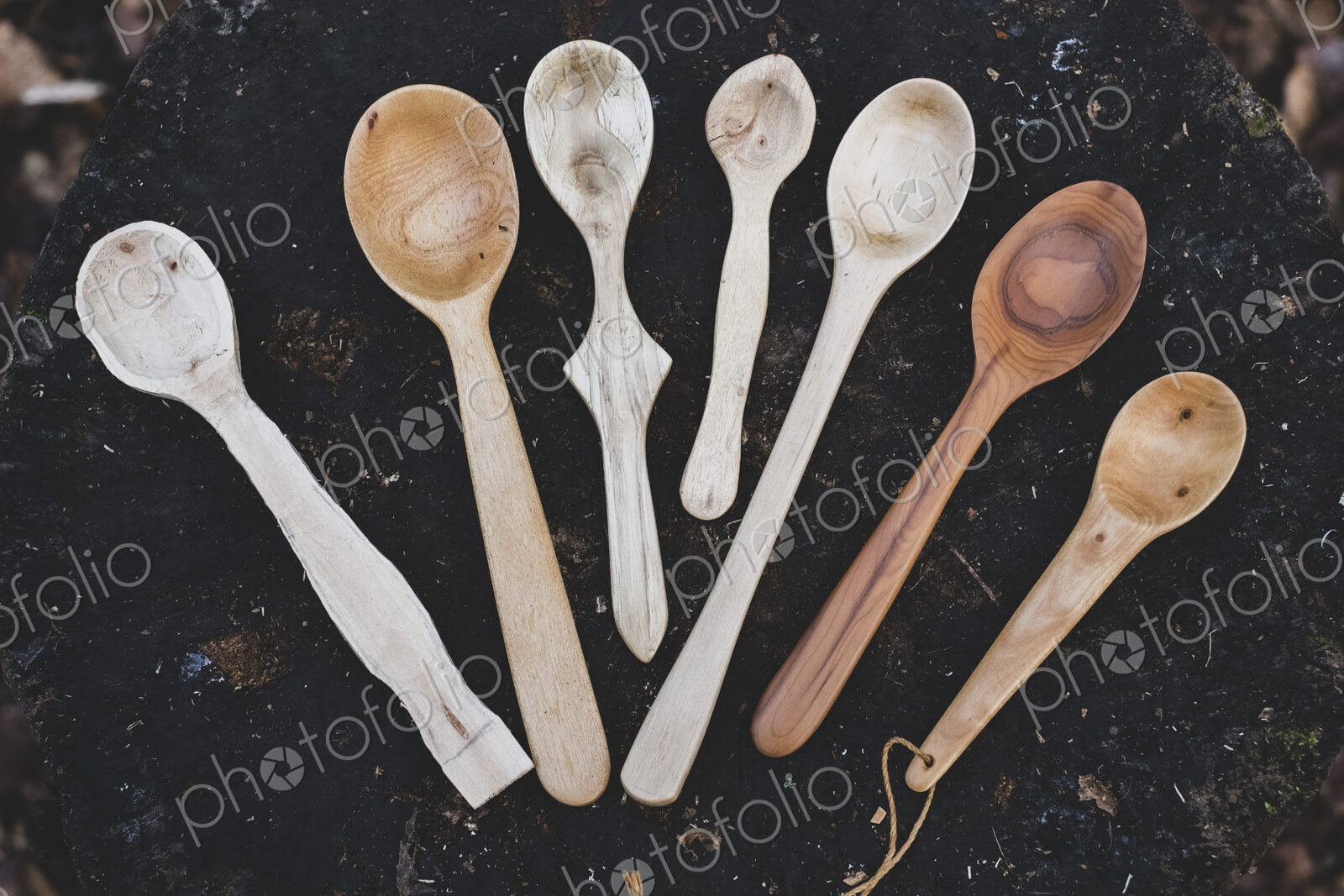 High angle close up of a selection of carved wooden spoons on chopping block.