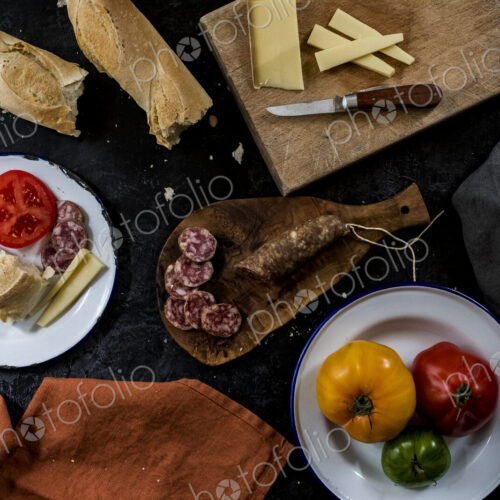 High angle close up of a selection of cheeses, tomatoes, salami and French baguette on… High angle close up of a selection of cheeses, tomatoes, salami and French baguette on…