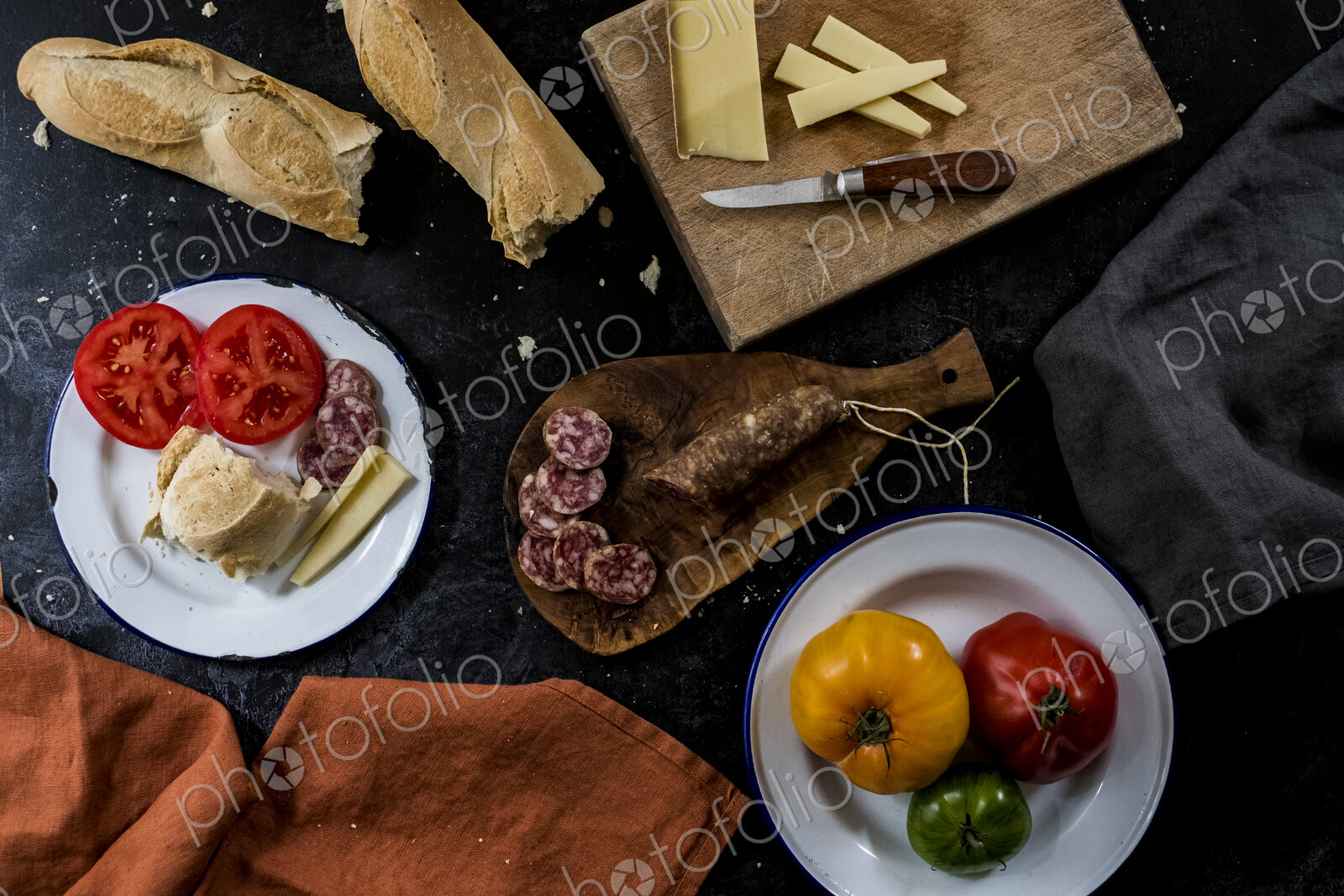 High angle close up of a selection of cheeses, tomatoes, salami and French baguette on…