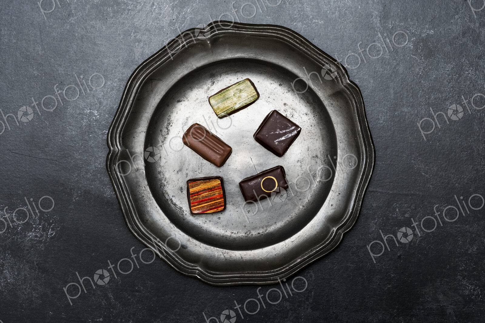 High angle close up of a selection of chocolate pralines on a tin plate on black…