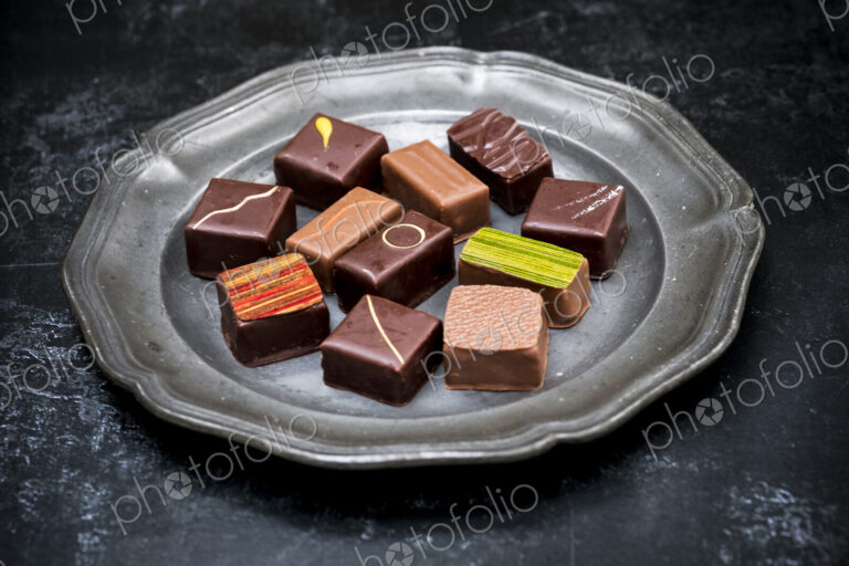 High angle close up of a selection of chocolate pralines on a tin plate on black…