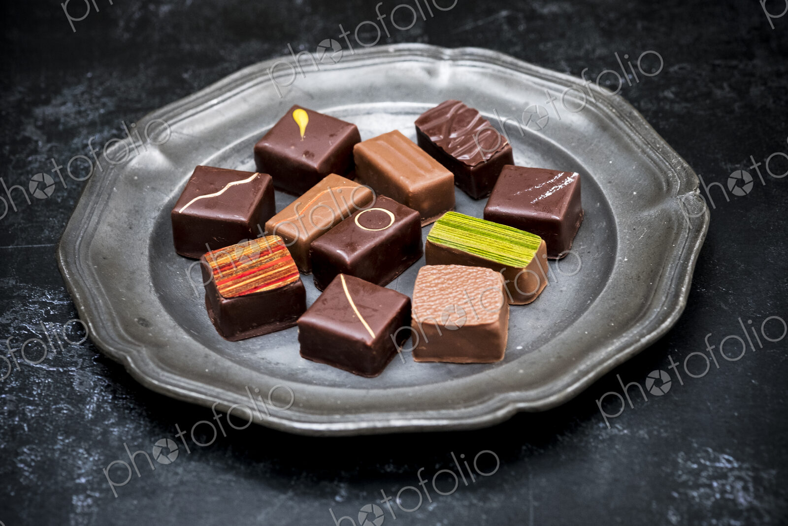 High angle close up of a selection of chocolate pralines on a tin plate on black…