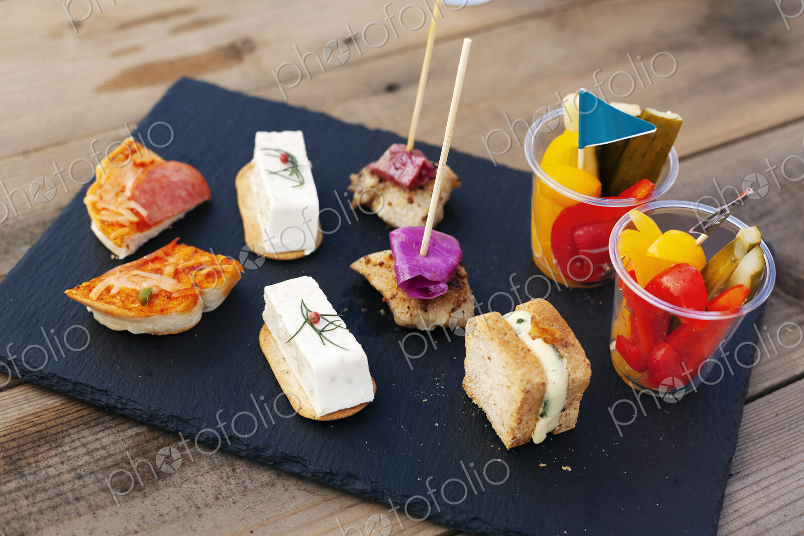 High angle close up of a selection of sandwiches and fresh vegetables on slate tray.