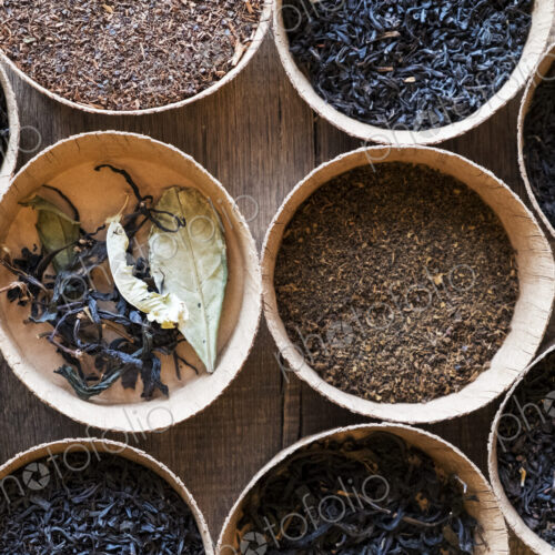 High angle close up of a selection of tea leaves in small wooden bowls.