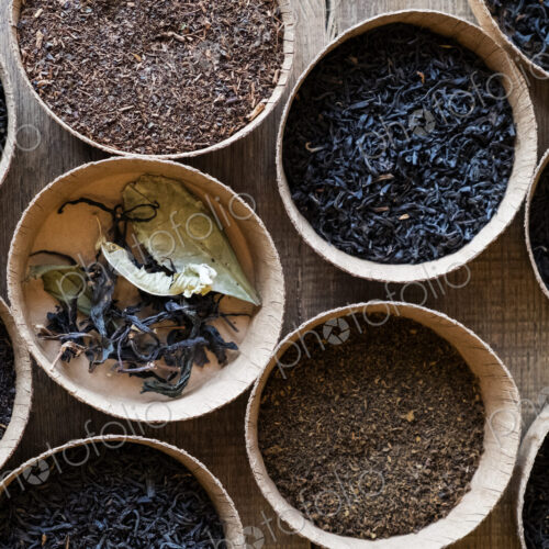 High angle close up of a selection of tea leaves in small wooden bowls.