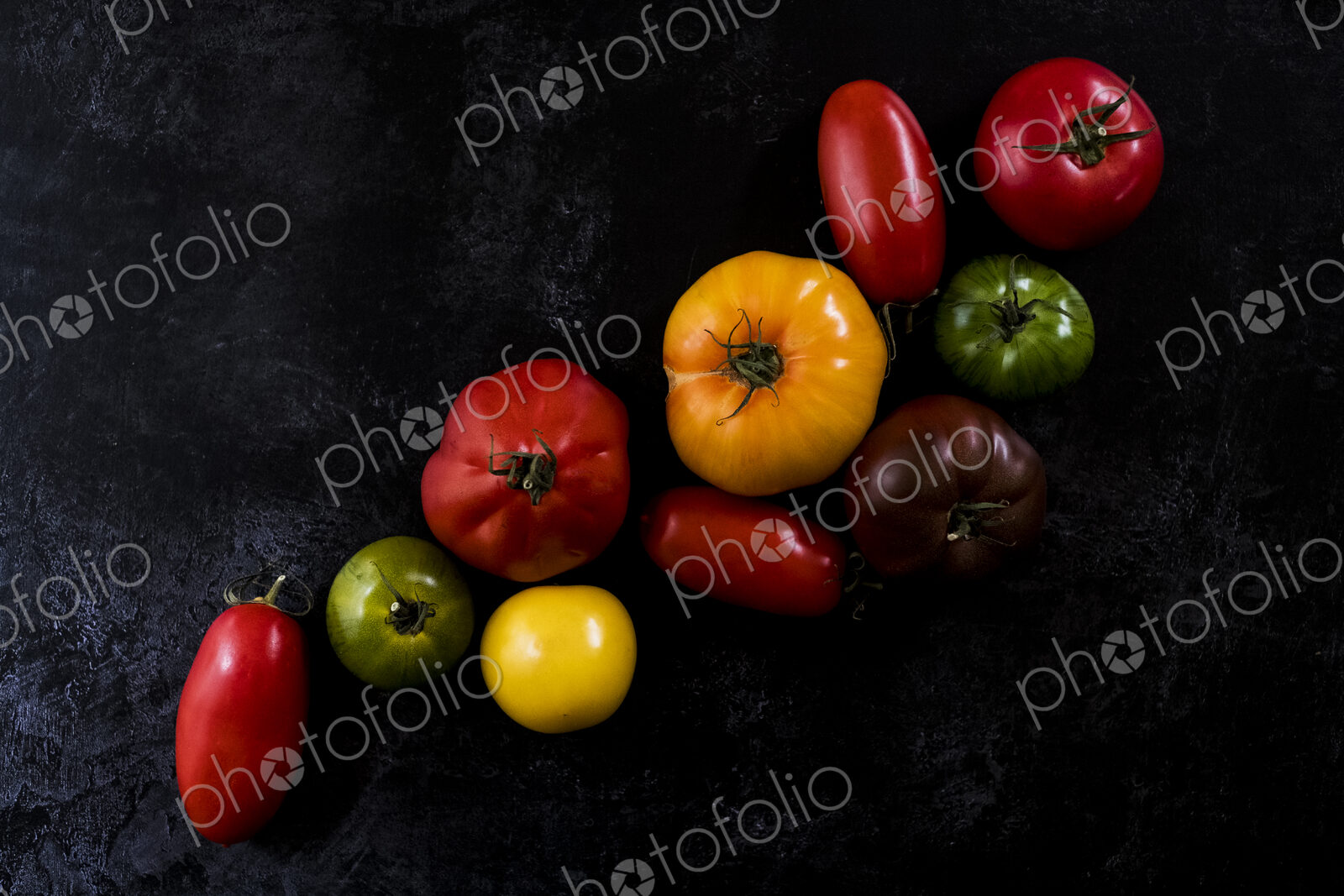 High angle close up of a selection of tomatoes in various shapes and colours on black…