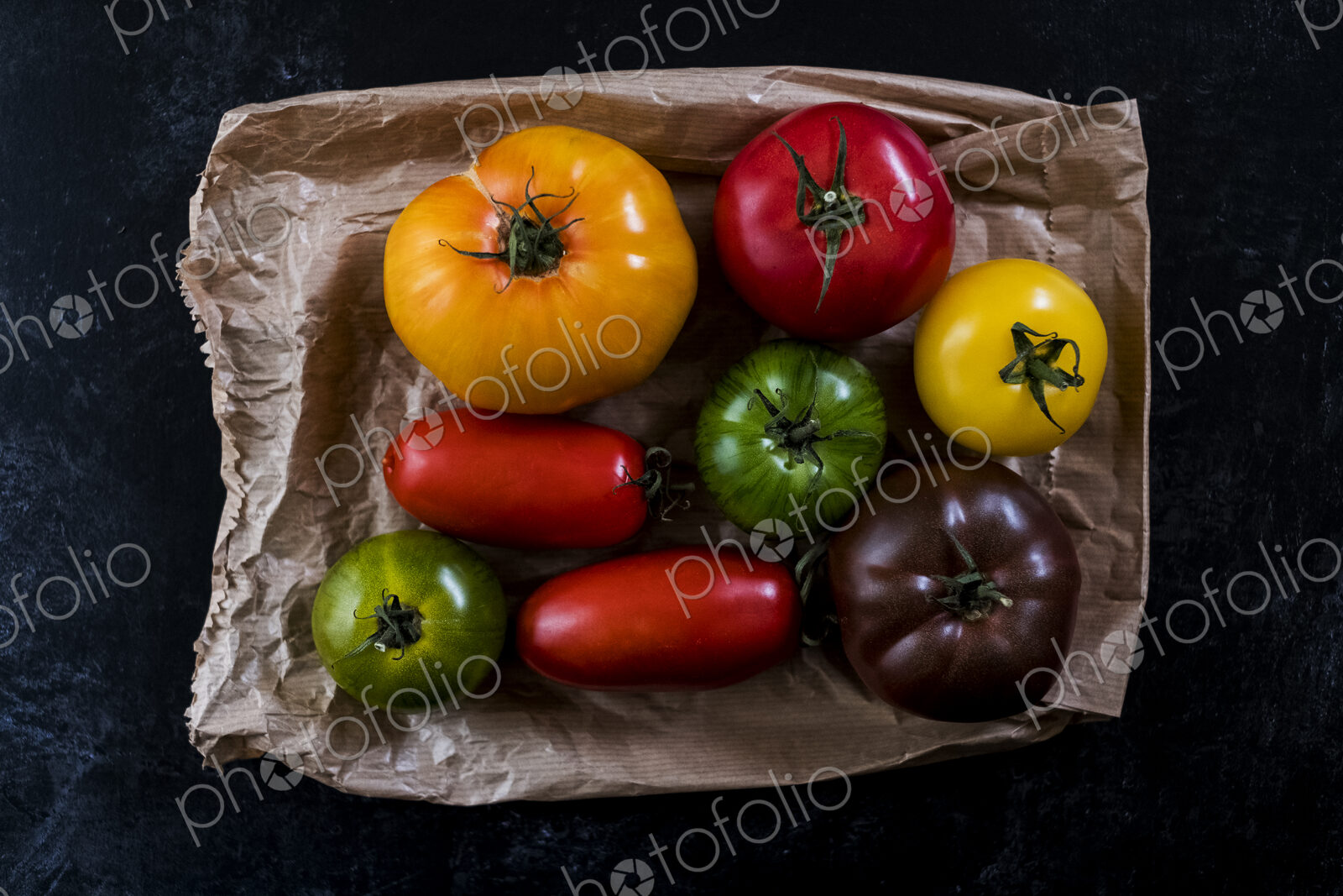 High angle close up of a selection of tomatoes in various shapes and colours on black…
