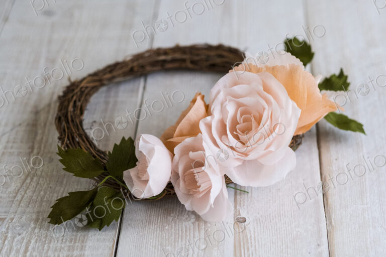 High angle close up of a small wreath with pale and salmon pink paper roses.