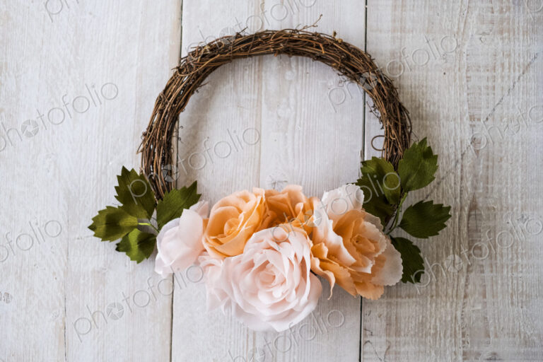 High angle close up of a small wreath with pale and salmon pink paper roses.