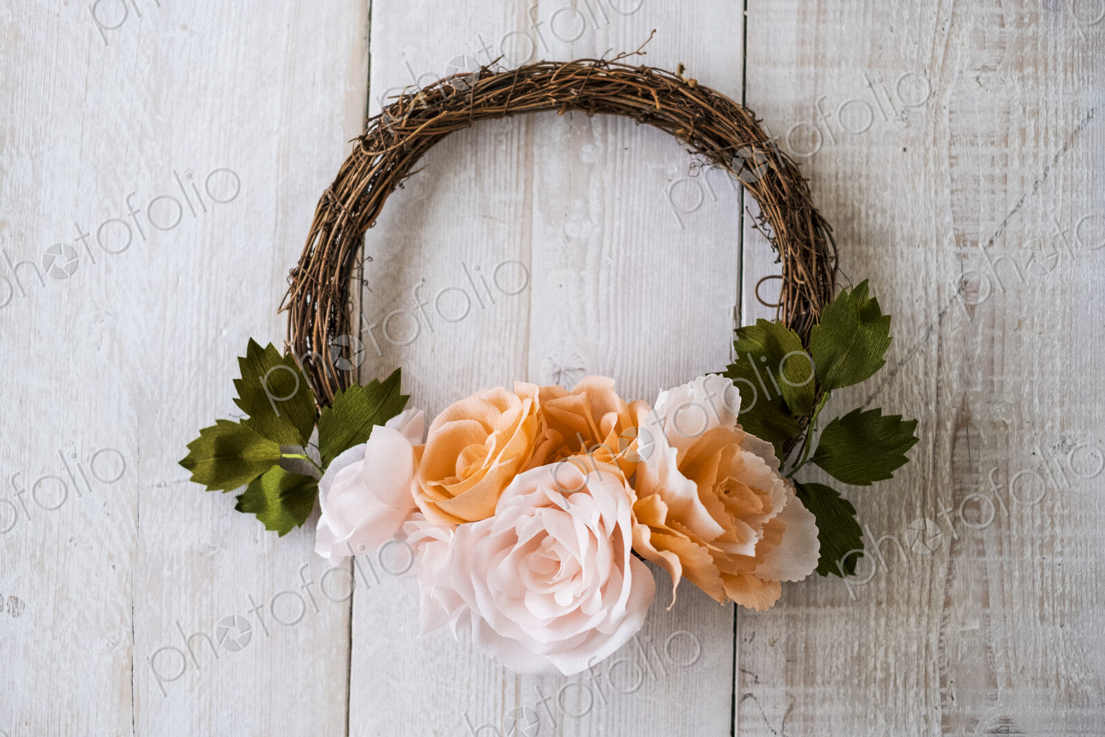 High angle close up of a small wreath with pale and salmon pink paper roses.