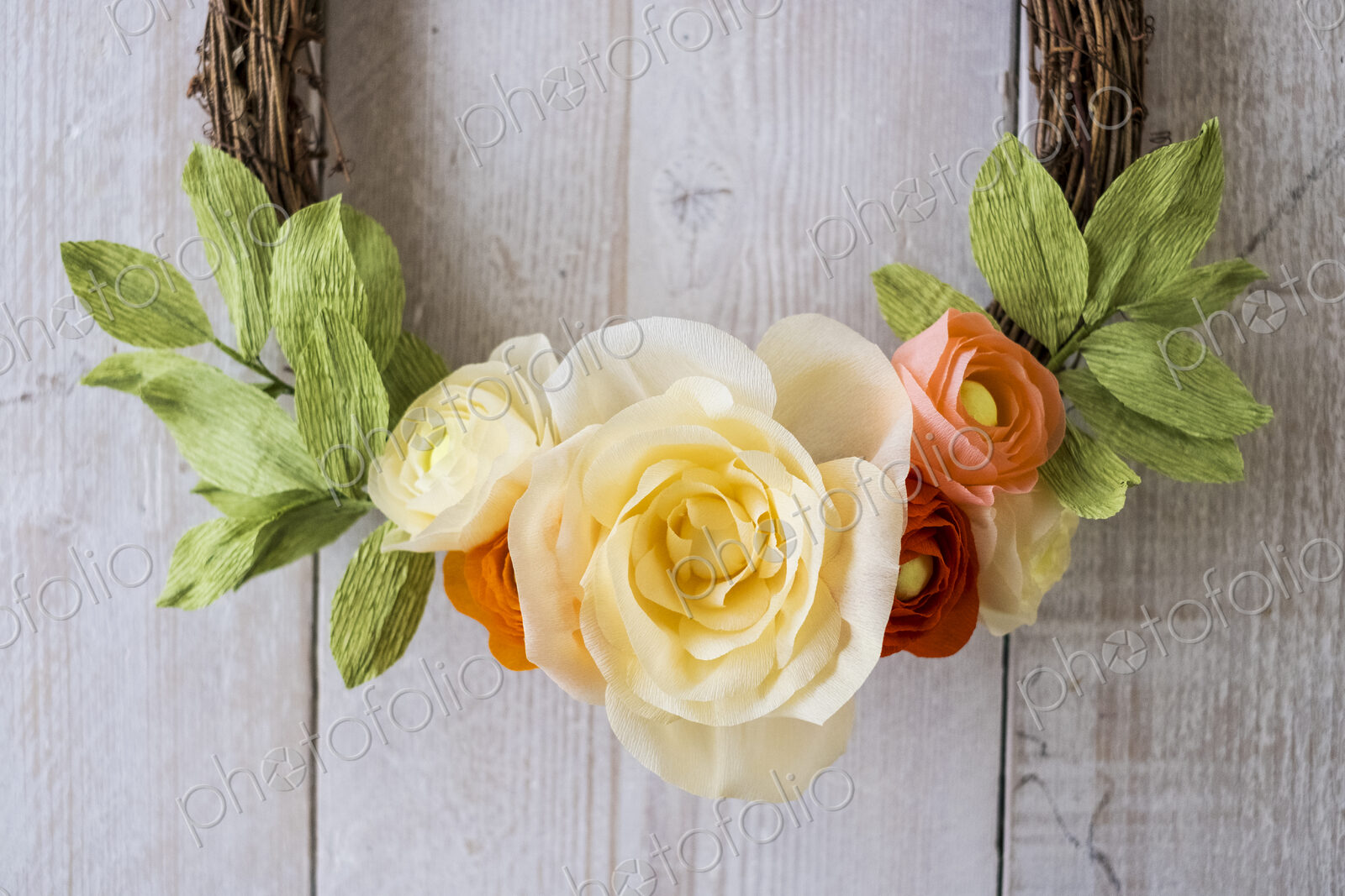 High angle close up of a small wreath with pale yellow and pink paper roses.