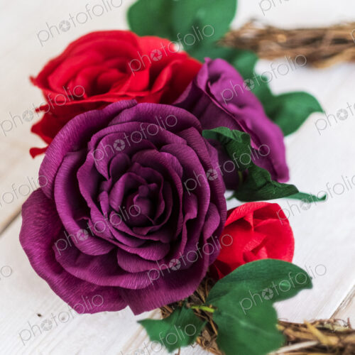 High angle close up of a small wreath with red and purple paper roses. High angle close up of a small wreath with red and purple paper roses.