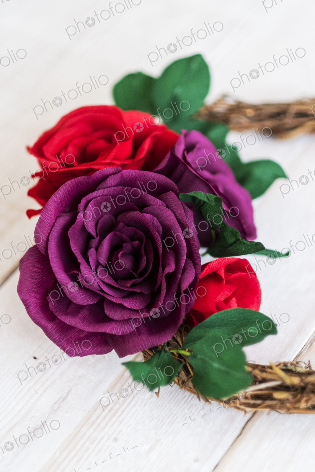 High angle close up of a small wreath with red and purple paper roses.