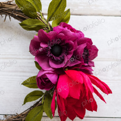 High angle close up of a small wreath with red and purple paper roses. High angle close up of a small wreath with red and purple paper roses.