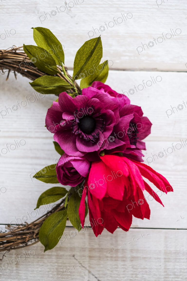 High angle close up of a small wreath with red and purple paper roses.
