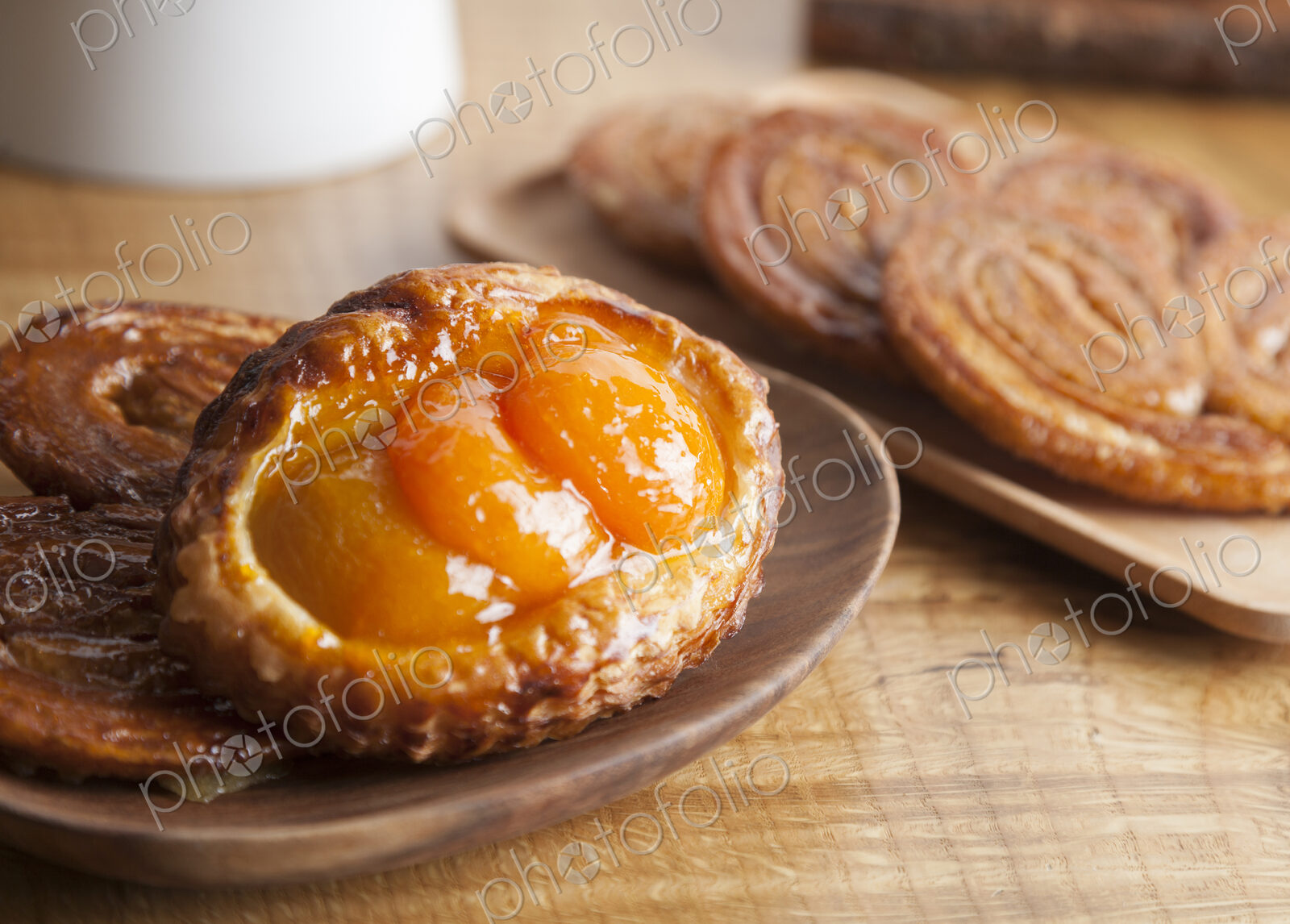 High angle close up of an apricot tart and sweet palmiers, baked goods on brown plates.