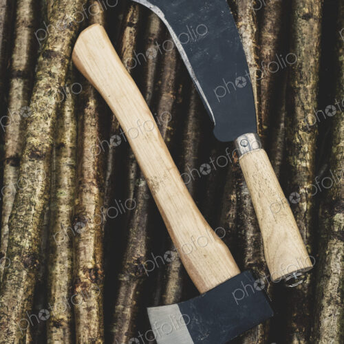 High angle close up of axe and bill hook lying on bunch of wooden stakes used in… High angle close up of axe and bill hook lying on bunch of wooden stakes used in…