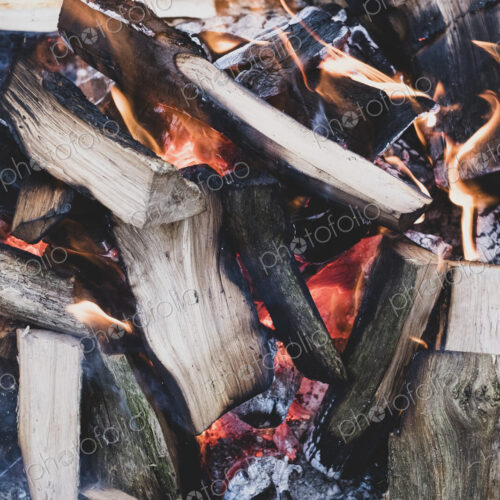 High angle close up of burning wooden logs of a campfire in a forest.