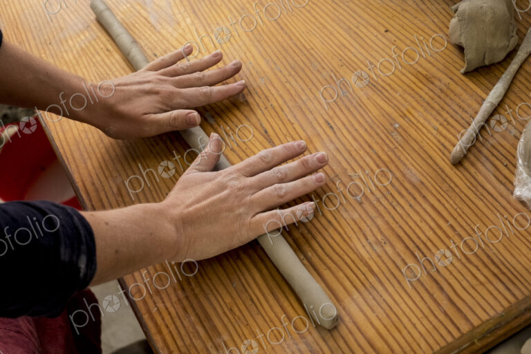 High angle close up of ceramic artist in her workshop, rolling out piece of clay on…