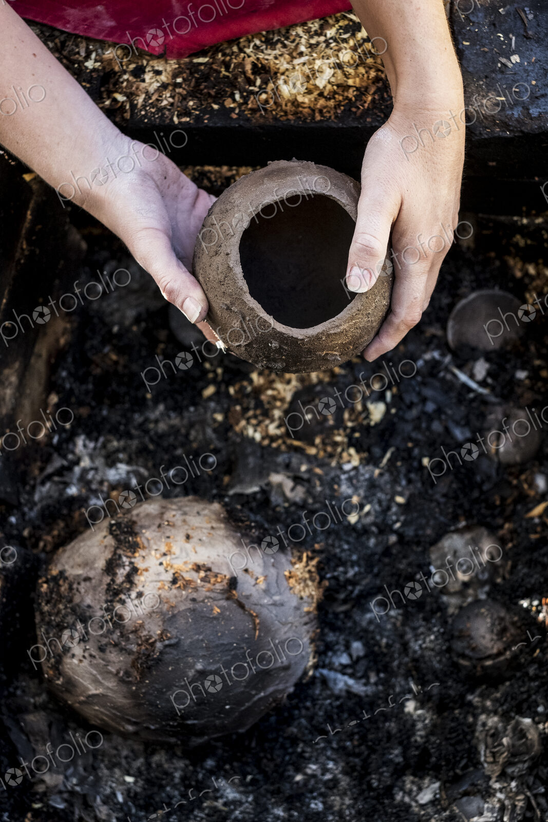 High angle close up of ceramic artist sitting next to outdoor smoke fire pit, working…