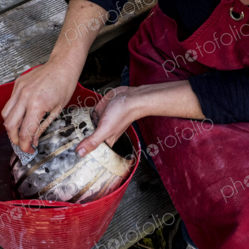 High angle close up of ceramic artist sitting next to red bucket with water, working…