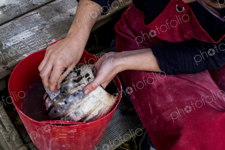 High angle close up of ceramic artist sitting next to red bucket with water, working…