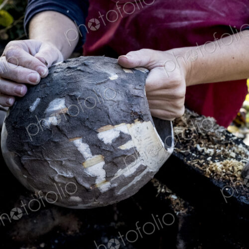 High angle close up of ceramic artist sitting outdoors, working on vase.