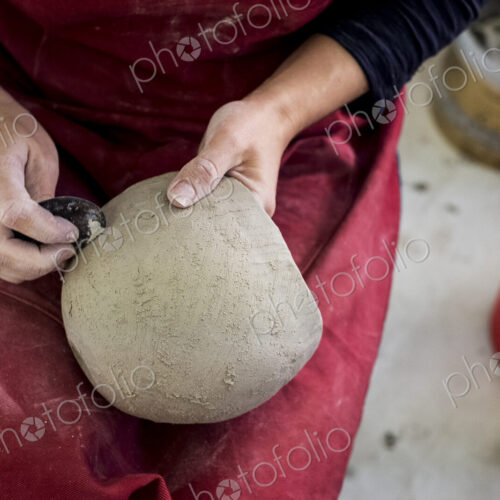 High angle close up of ceramic artist wearing red apron sitting in her workshop,…