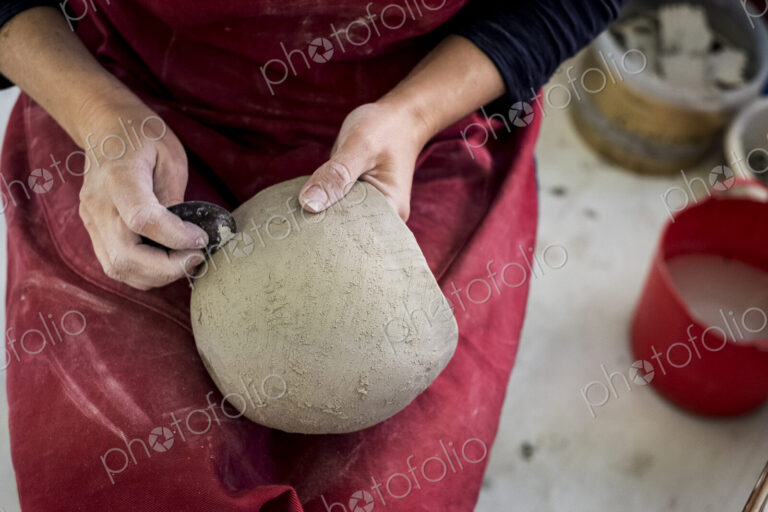 High angle close up of ceramic artist wearing red apron sitting in her workshop,…