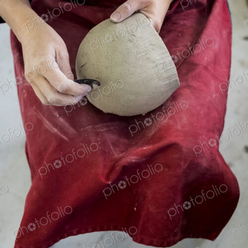 High angle close up of ceramic artist wearing red apron sitting in her workshop,…