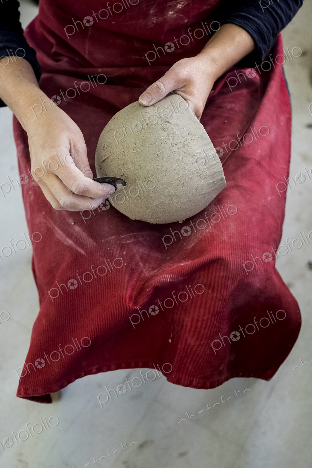 High angle close up of ceramic artist wearing red apron sitting in her workshop,…
