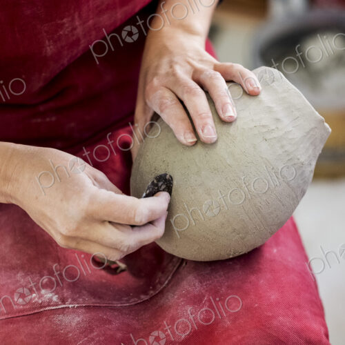 High angle close up of ceramic artist wearing red apron sitting in her workshop,…