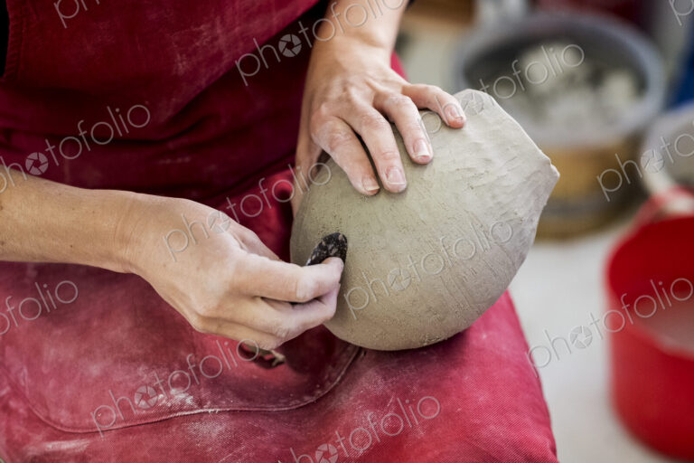 High angle close up of ceramic artist wearing red apron sitting in her workshop,…