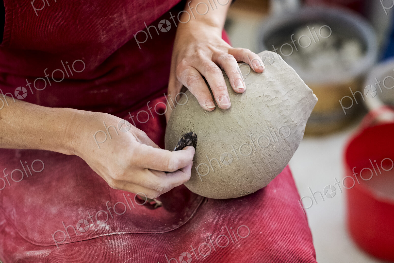 High angle close up of ceramic artist wearing red apron sitting in her workshop,…