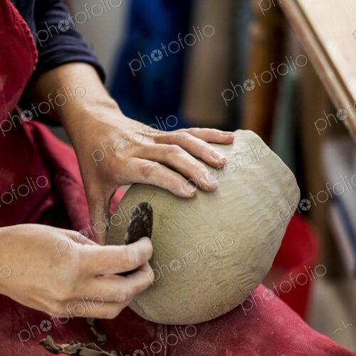 High angle close up of ceramic artist wearing red apron sitting in her workshop,…