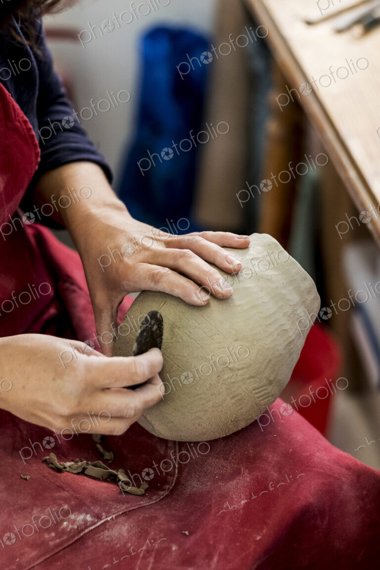 High angle close up of ceramic artist wearing red apron sitting in her workshop,…