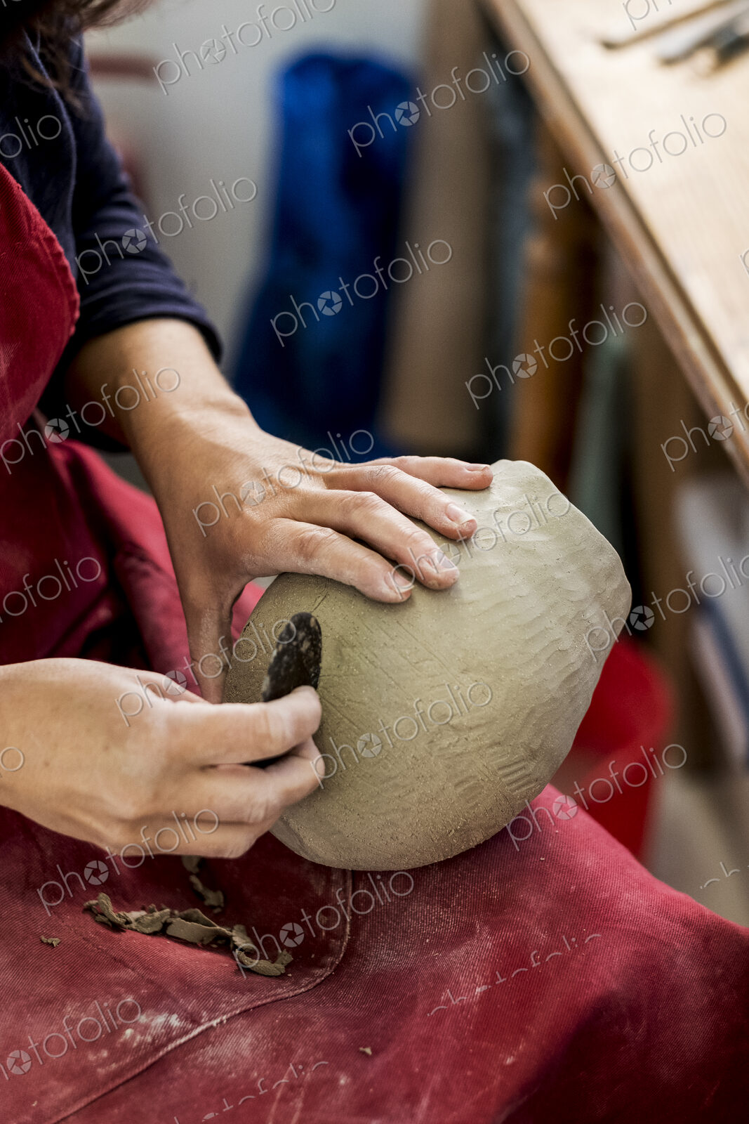 High angle close up of ceramic artist wearing red apron sitting in her workshop,…