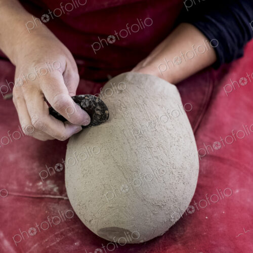 High angle close up of ceramic artist wearing red apron sitting in her workshop,…