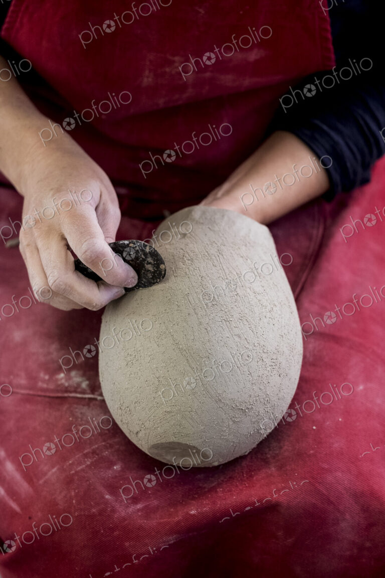 High angle close up of ceramic artist wearing red apron sitting in her workshop,…