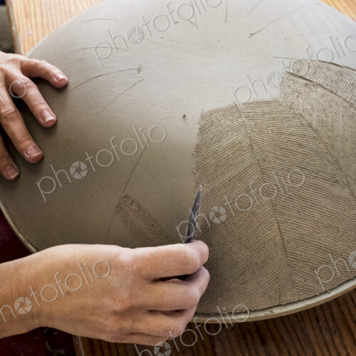 High angle close up of ceramic artist working on clay bowl, applying pattern with hand…