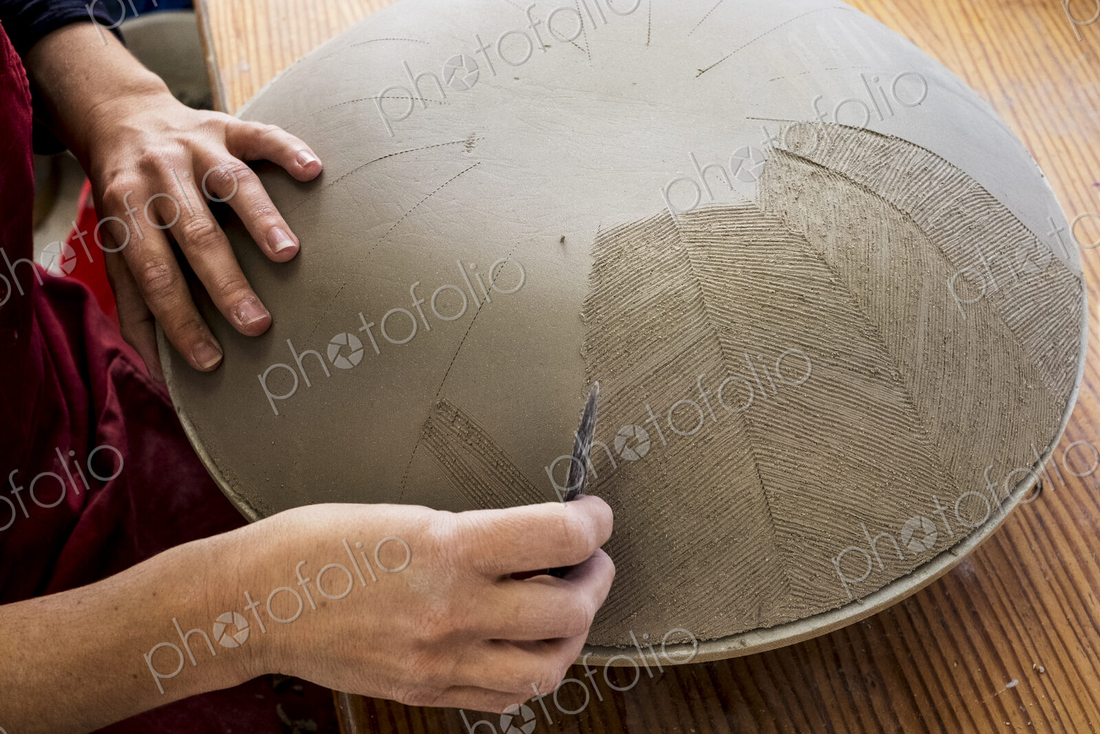 High angle close up of ceramic artist working on clay bowl, applying pattern with hand…