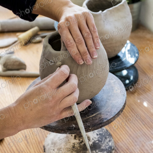 High angle close up of ceramic artist working on clay vase using pottery tool.