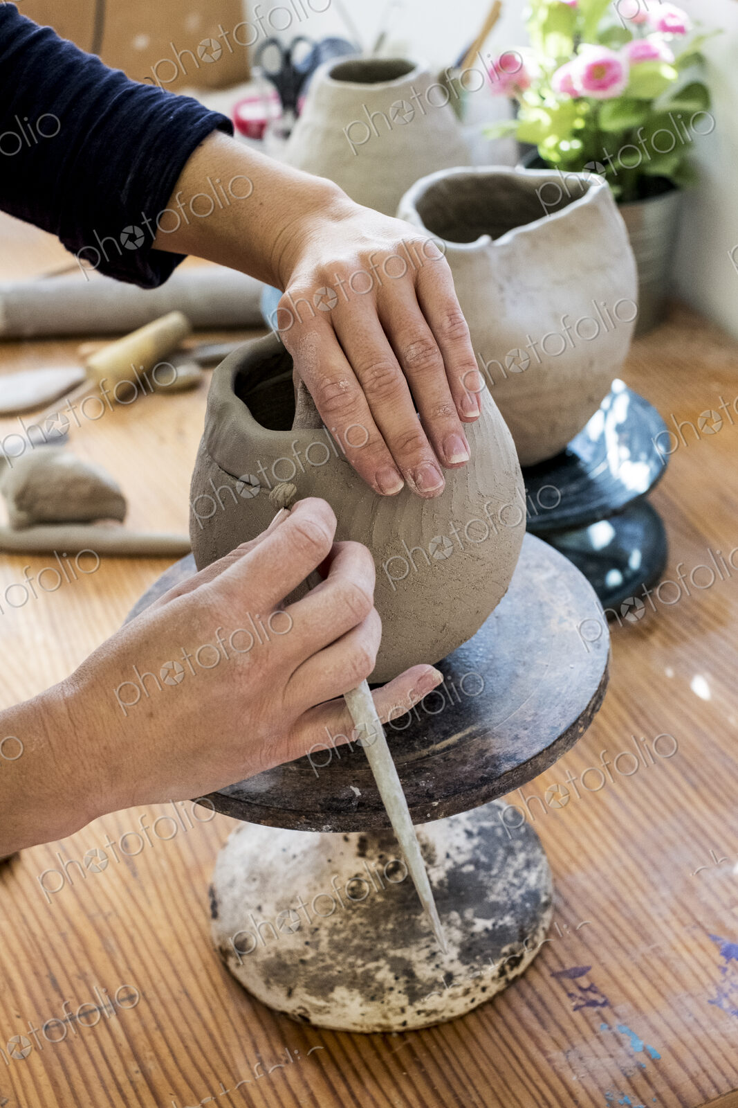 High angle close up of ceramic artist working on clay vase using pottery tool.