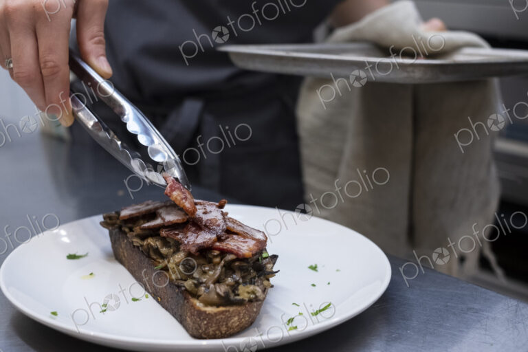 High angle close up of chef preparing toasted bread with bacon and mushrooms in an…