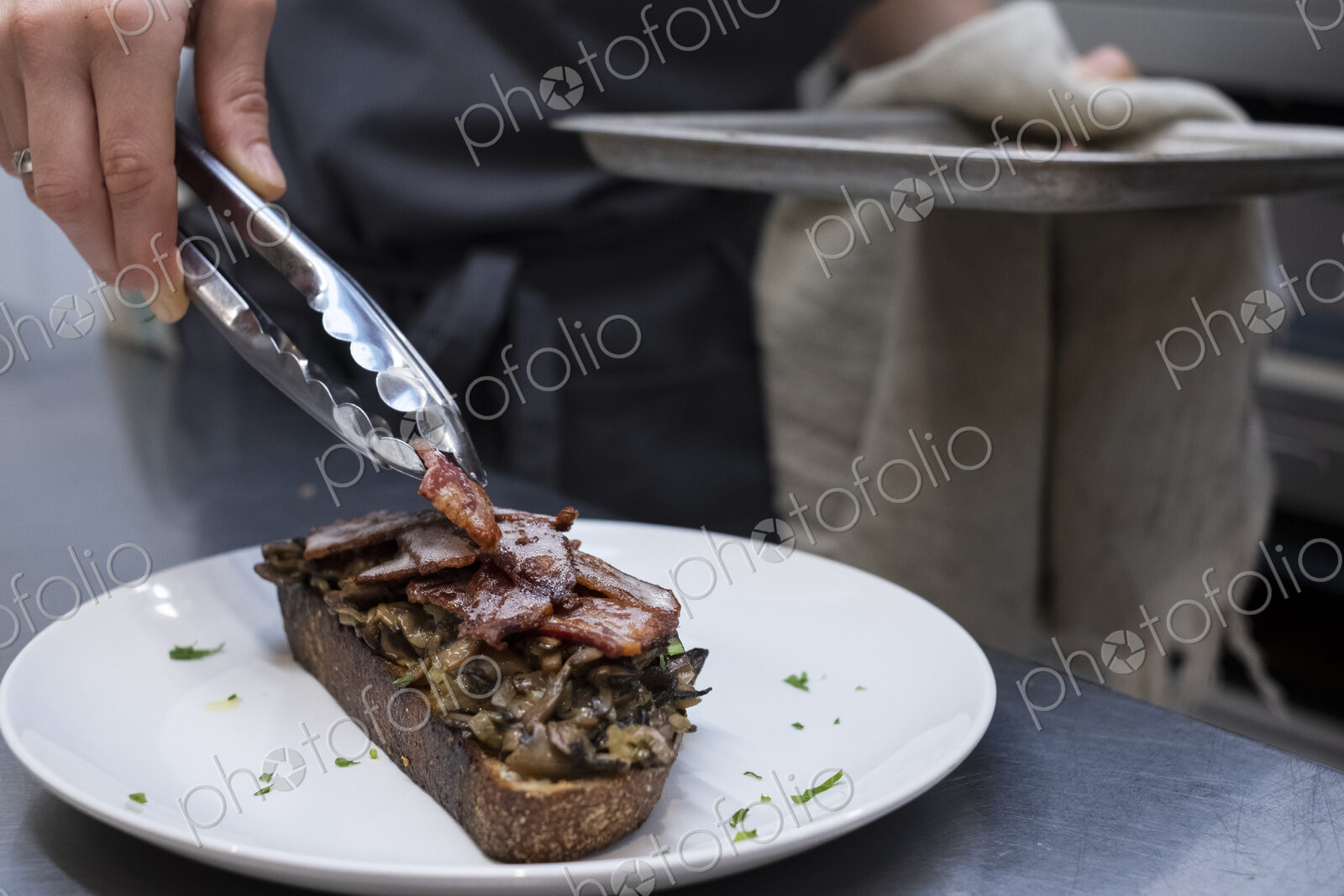 High angle close up of chef preparing toasted bread with bacon and mushrooms in an…