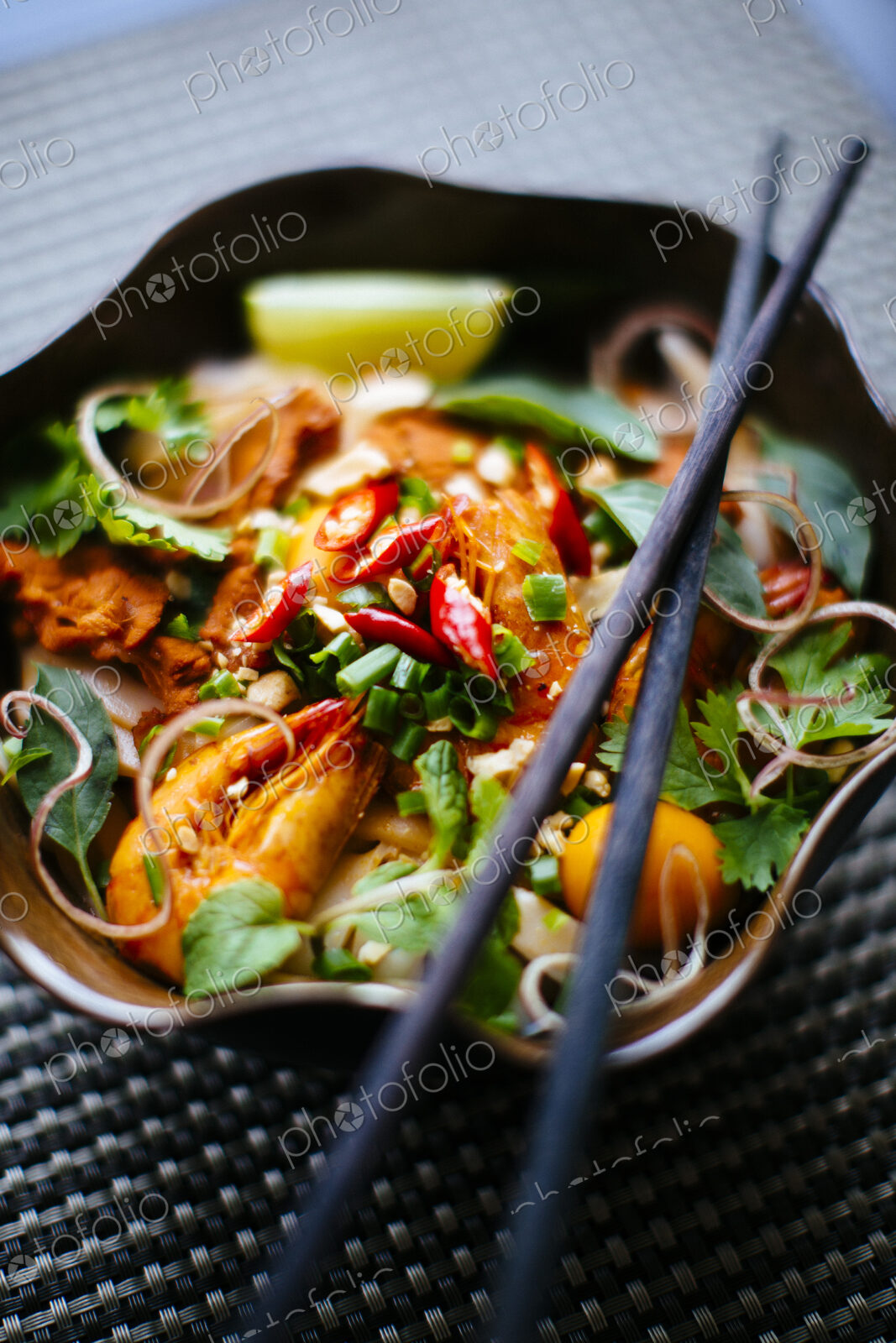 High angle close up of chopsticks on bowl with Asian food containing noodles, prawns,…